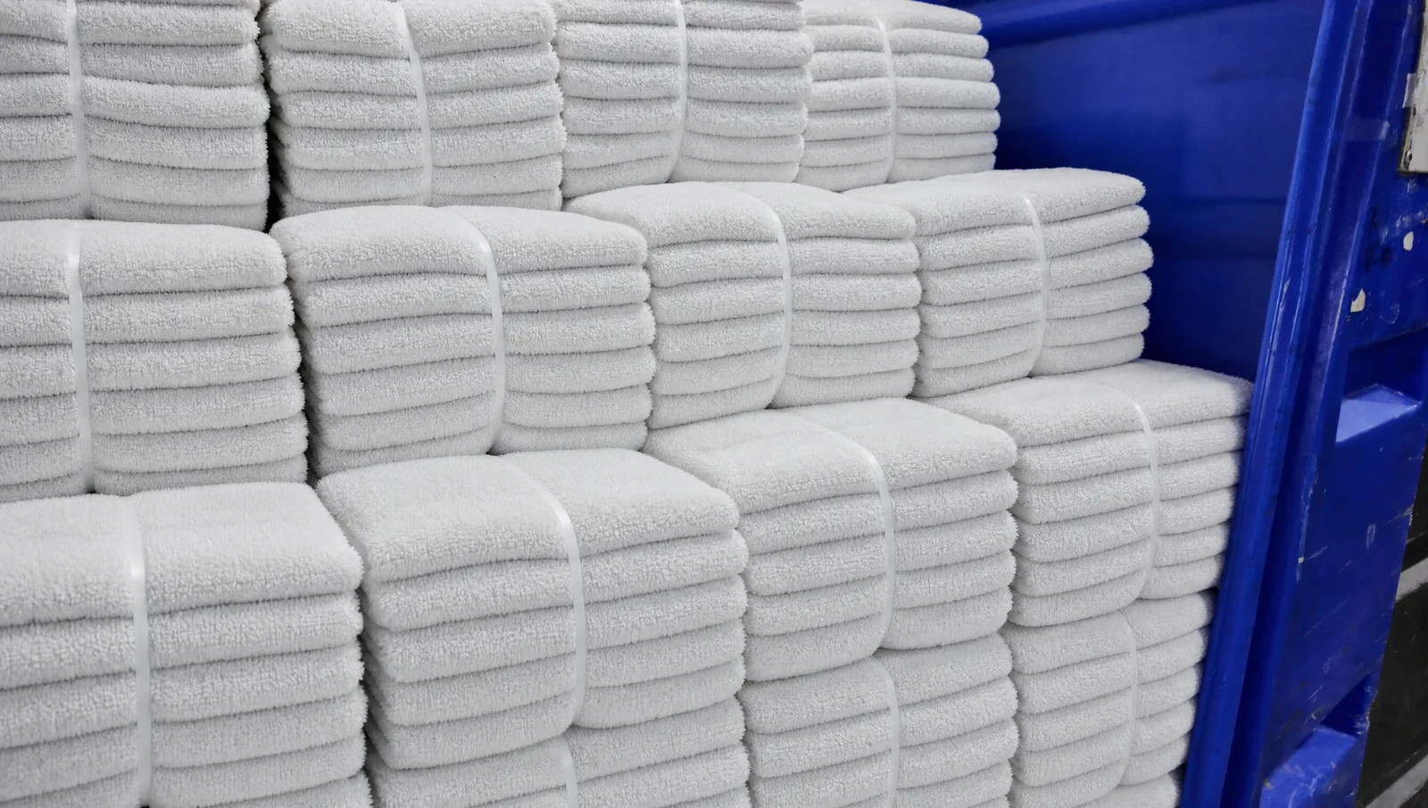 Clean white towels bundled and stacked in a blue laundry cart